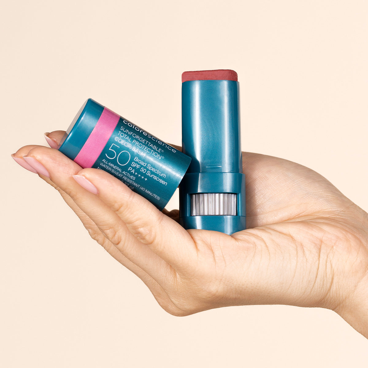 Hand holding two blue sunscreen sticks with a beige background