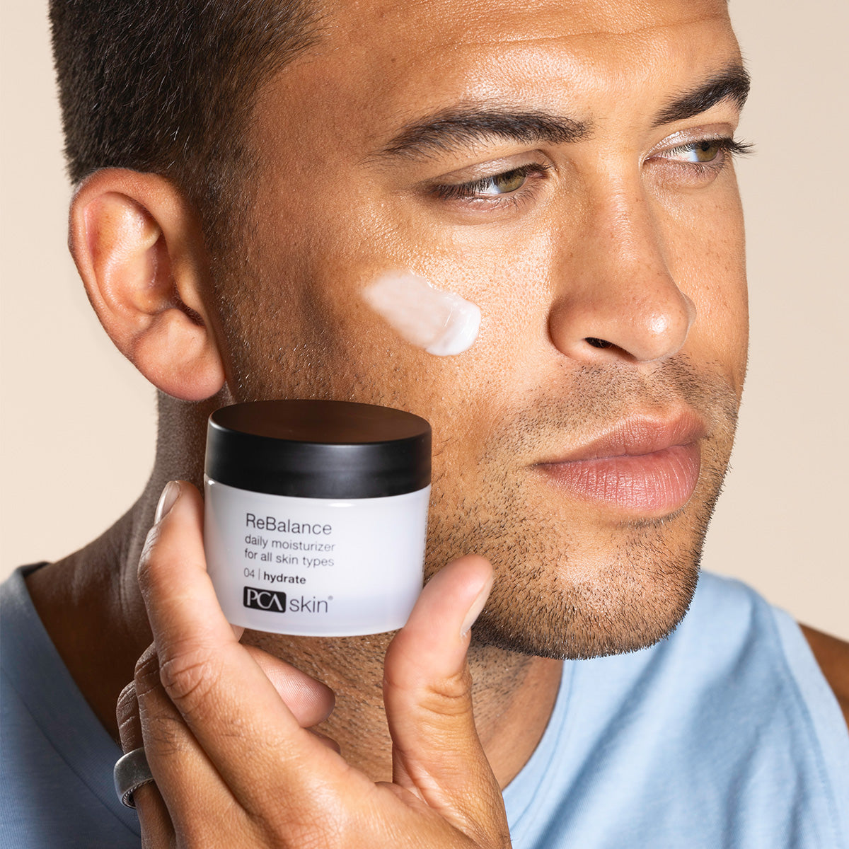 Man holding PCA Skin rebalance product with a swatch on his skin wearing a light blue shirt.