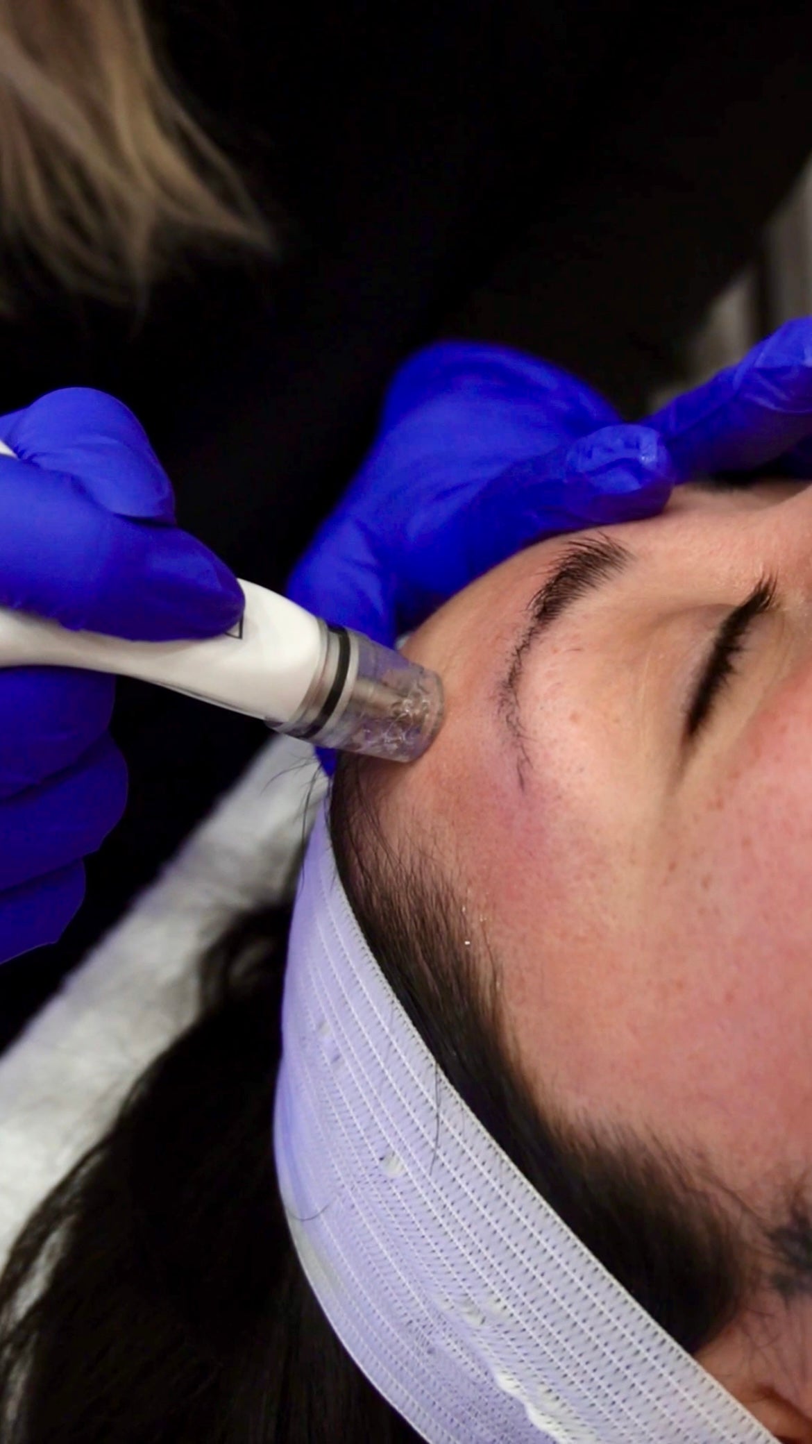 Person receiving a facial treatment with a device on their face, wearing gloves.