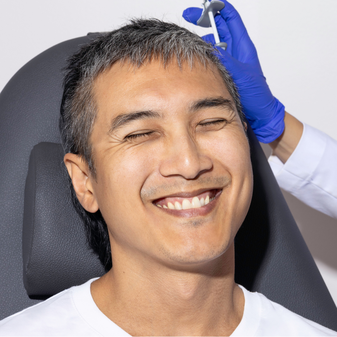 Man receiving a facial injection with a gloved hand holding a syringe against a white background