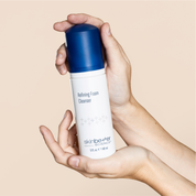 Hand holding a bottle of SkinCeuticals Refining Foam Cleanser against a beige background