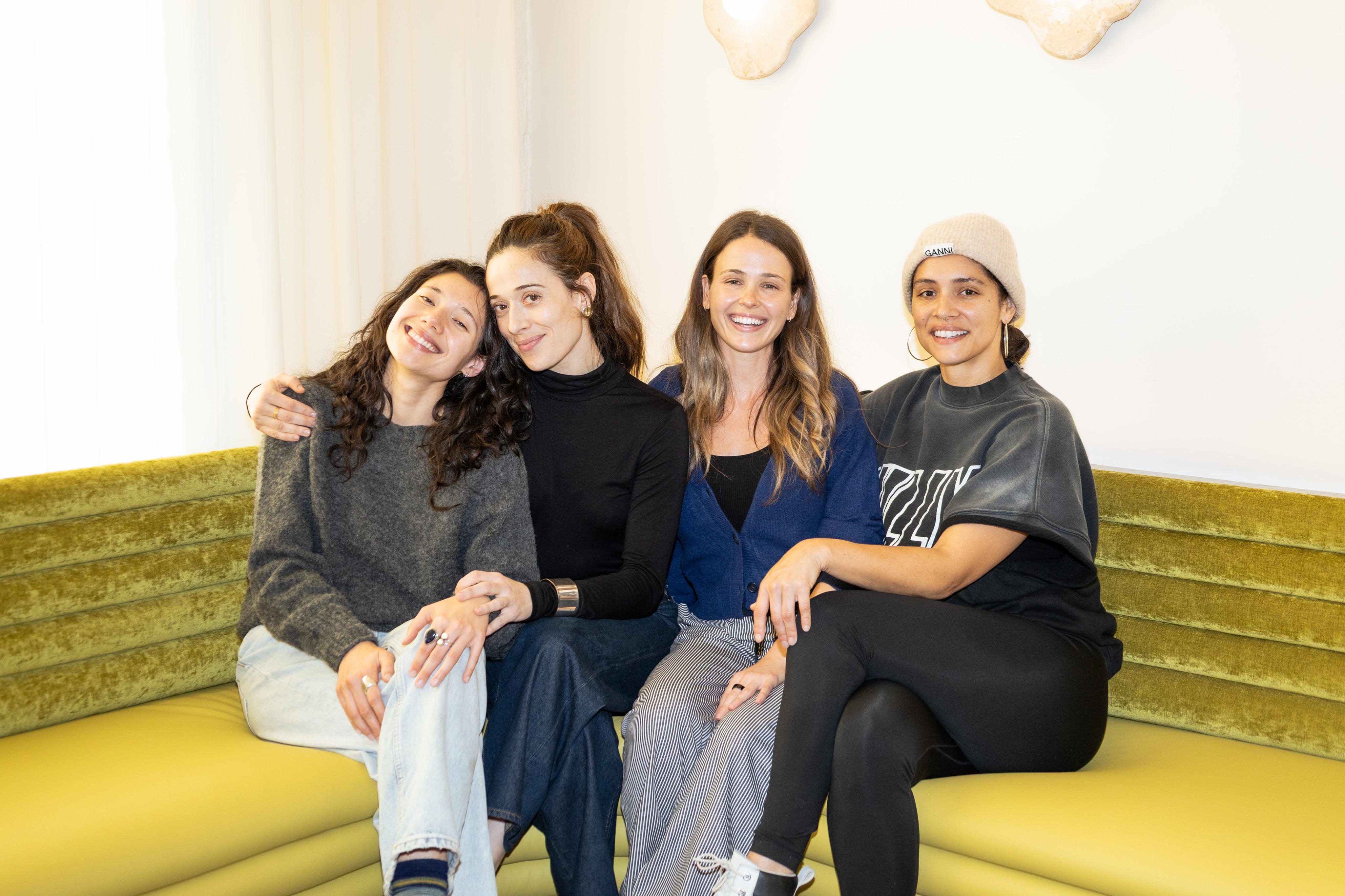 Four women sitting together on a yellow couch in a well-lit room.