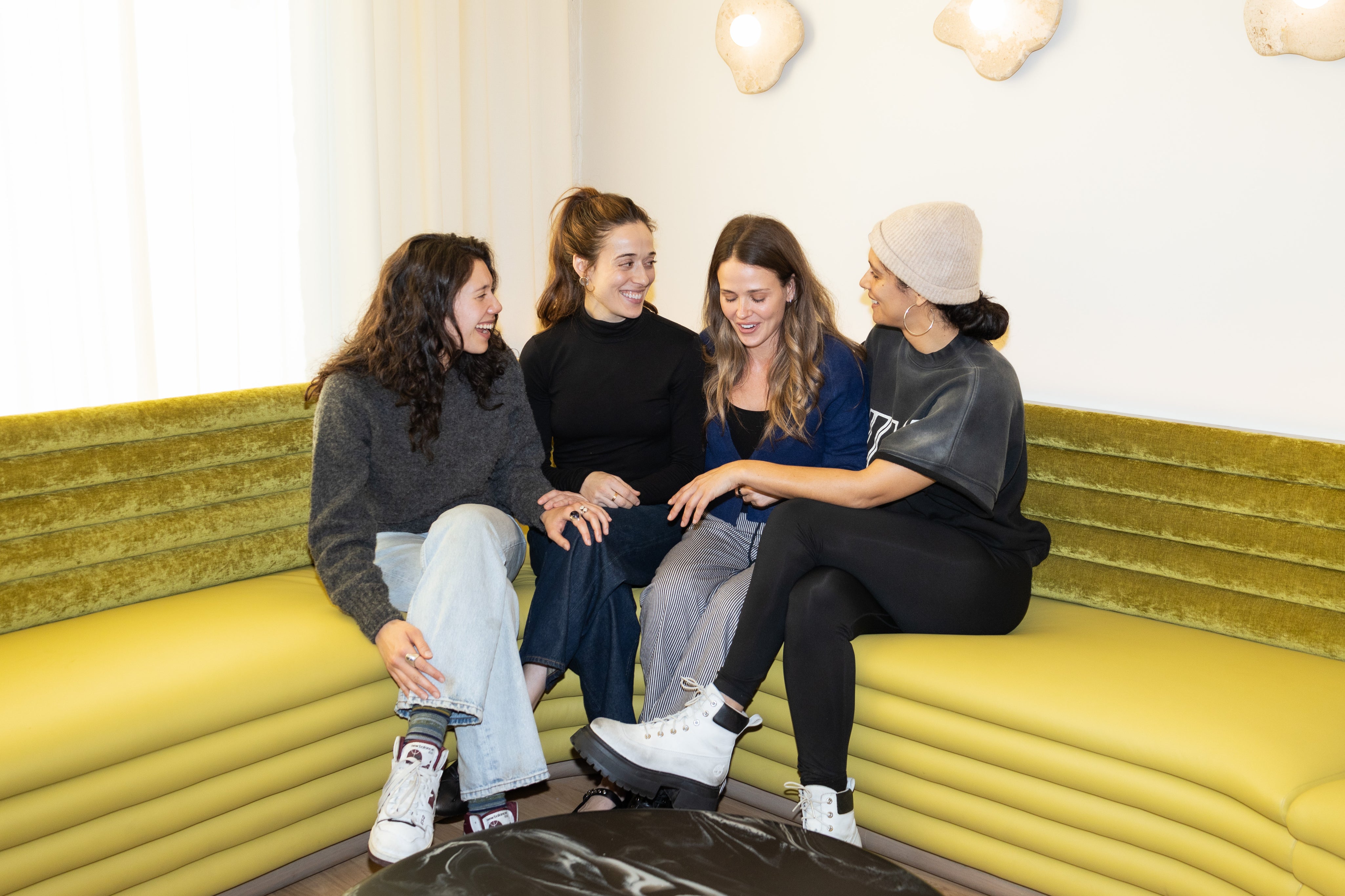 Four women sitting on a yellow couch in a modern indoor setting