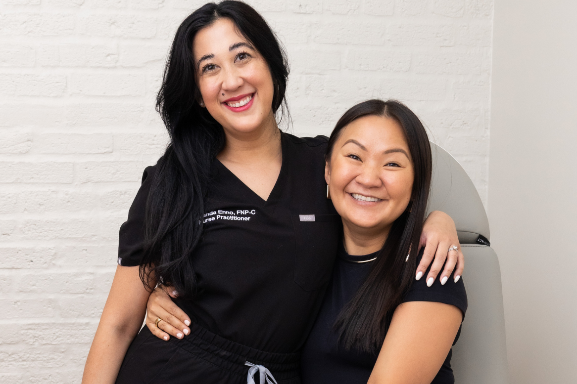 Two women in black shirts posing for a photo against a white brick wall.