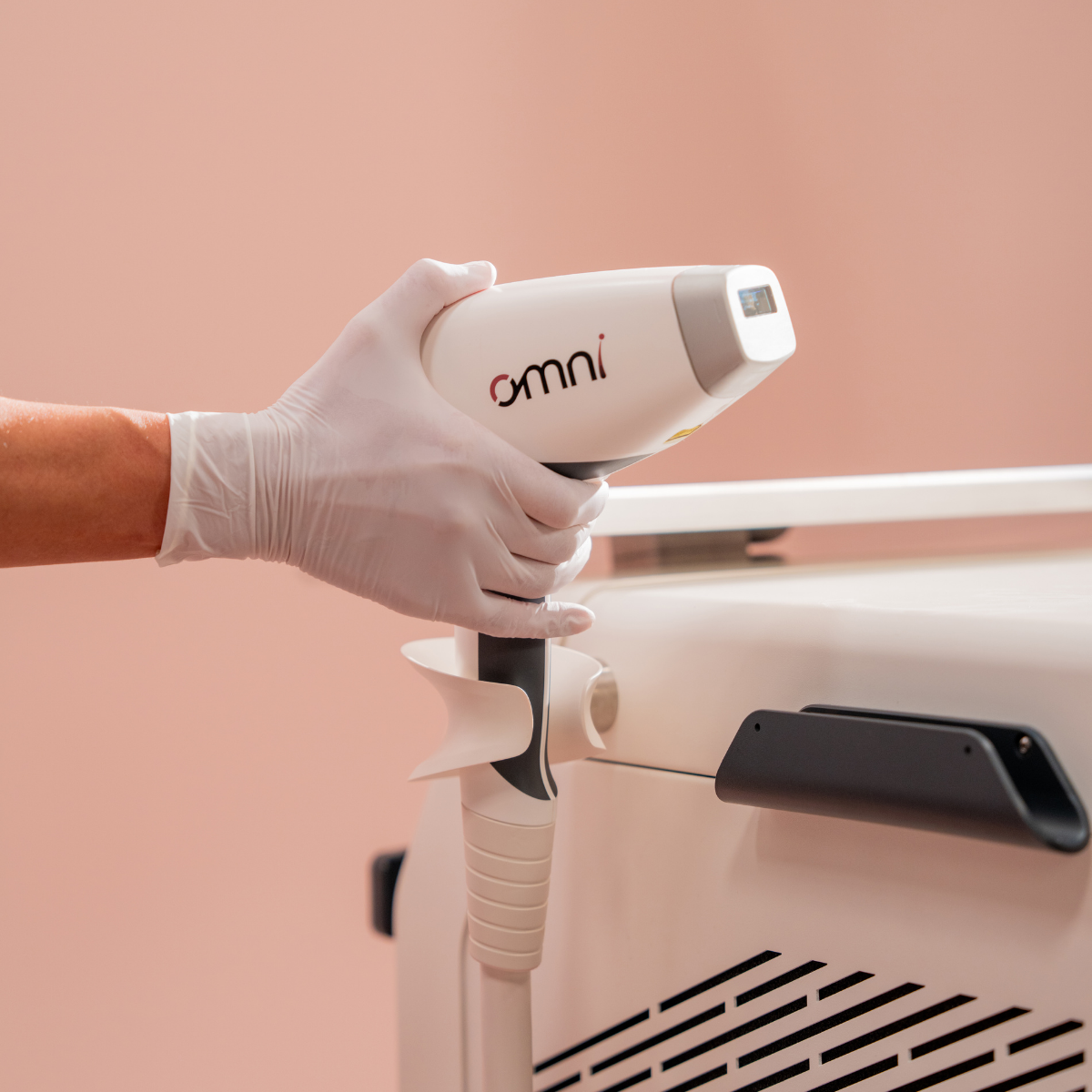 Hand wearing a white glove holding an 'omni' device against a beige background